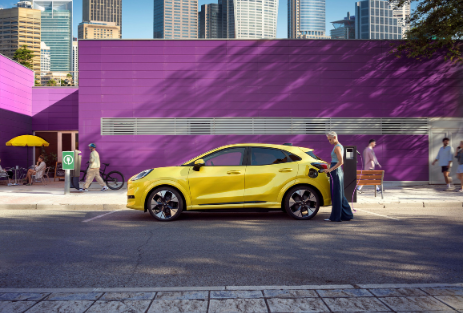 Angebot Ford Puma Gen-E | Jochem Gruppe Angebot Ford Puma Gen-E | Jochem Gruppe | Das Bild zeigt einen gelben PKW in der Stadt vor einer pinkfarbenen Mauer.