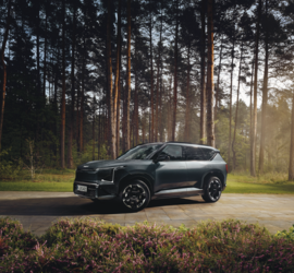 Kia EV 5 | Das Bild zeigt einen grauen SUV auf einem Waldparkplatz.