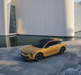 Kia K4 | Das Bild zeigt einen gelben Pkw vor einem modernen Gebäude.