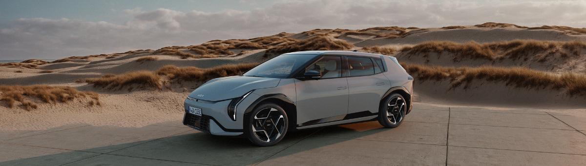 Kia EV4 | Das Bild zeigt einen hellblauen SUV auf einem Parkplatz vor Sanddünen.