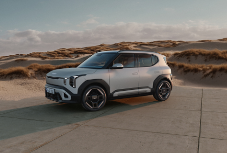 Kia EV2 | Das Bild zeigt einen hellblauen SUV auf einem Parkplatz vor Sanddünen.