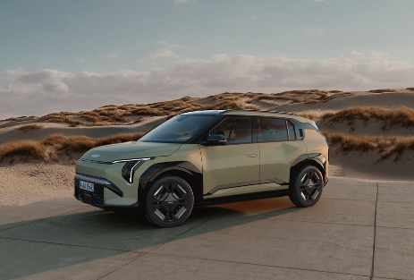 Kia EV3 | Das Bild zeigt einen hellblauen SUV auf einem Parkplatz vor Sanddünen.