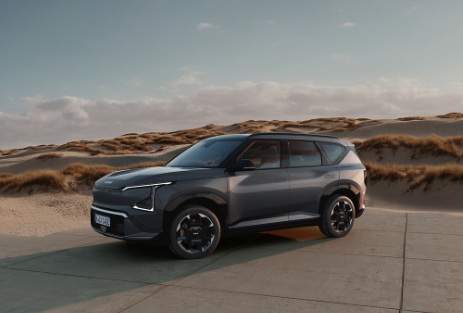 Kia EV5 | Das Bild zeigt einen hellblauen SUV auf einem Parkplatz vor Sanddünen.